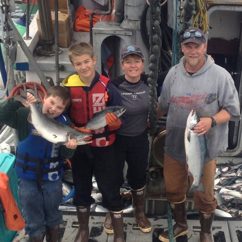 Four people on a boat deck holding fish with a large catch of fish around them.
