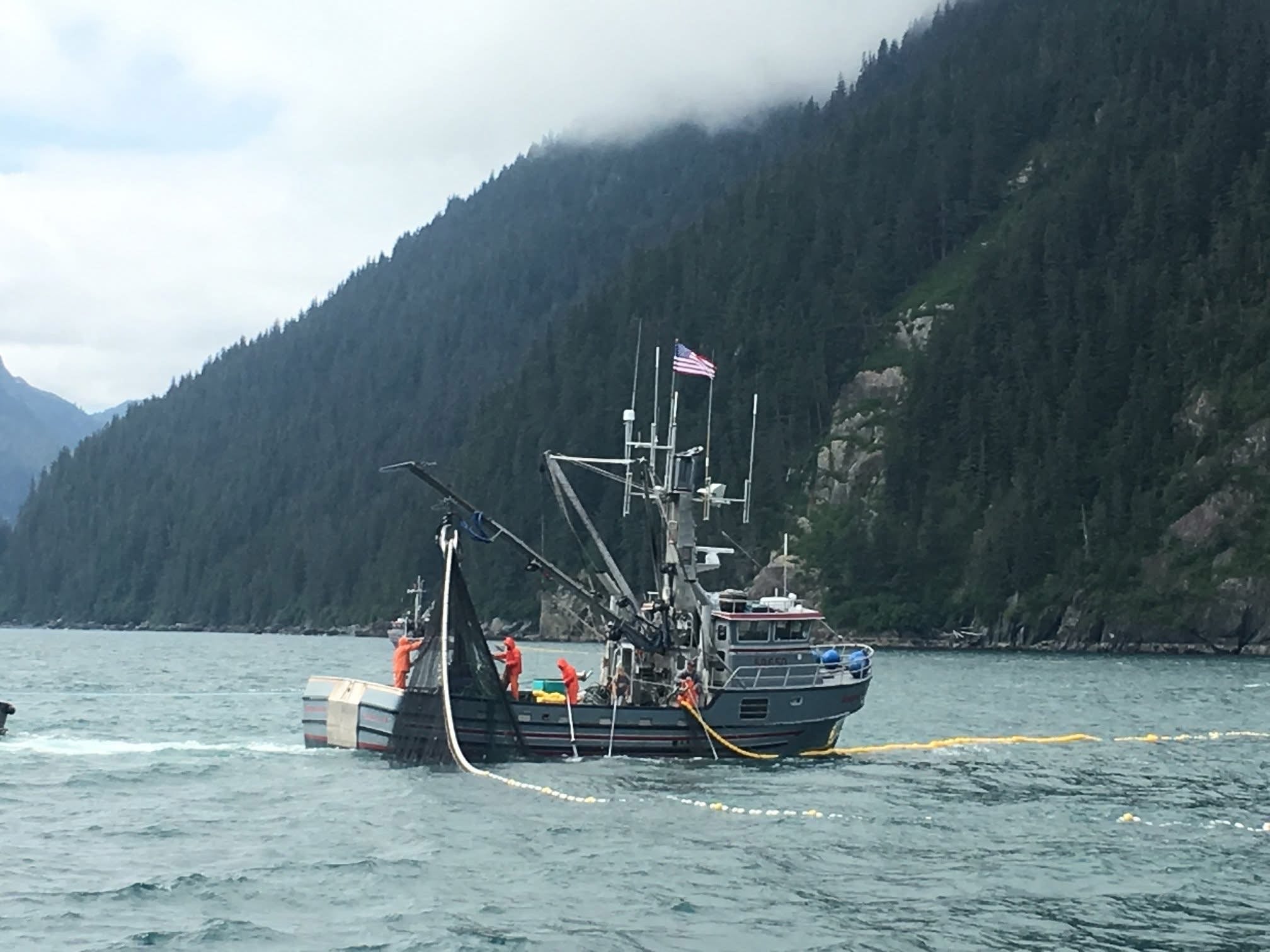Fishing boat with crew members on a body of water with mountains in the background