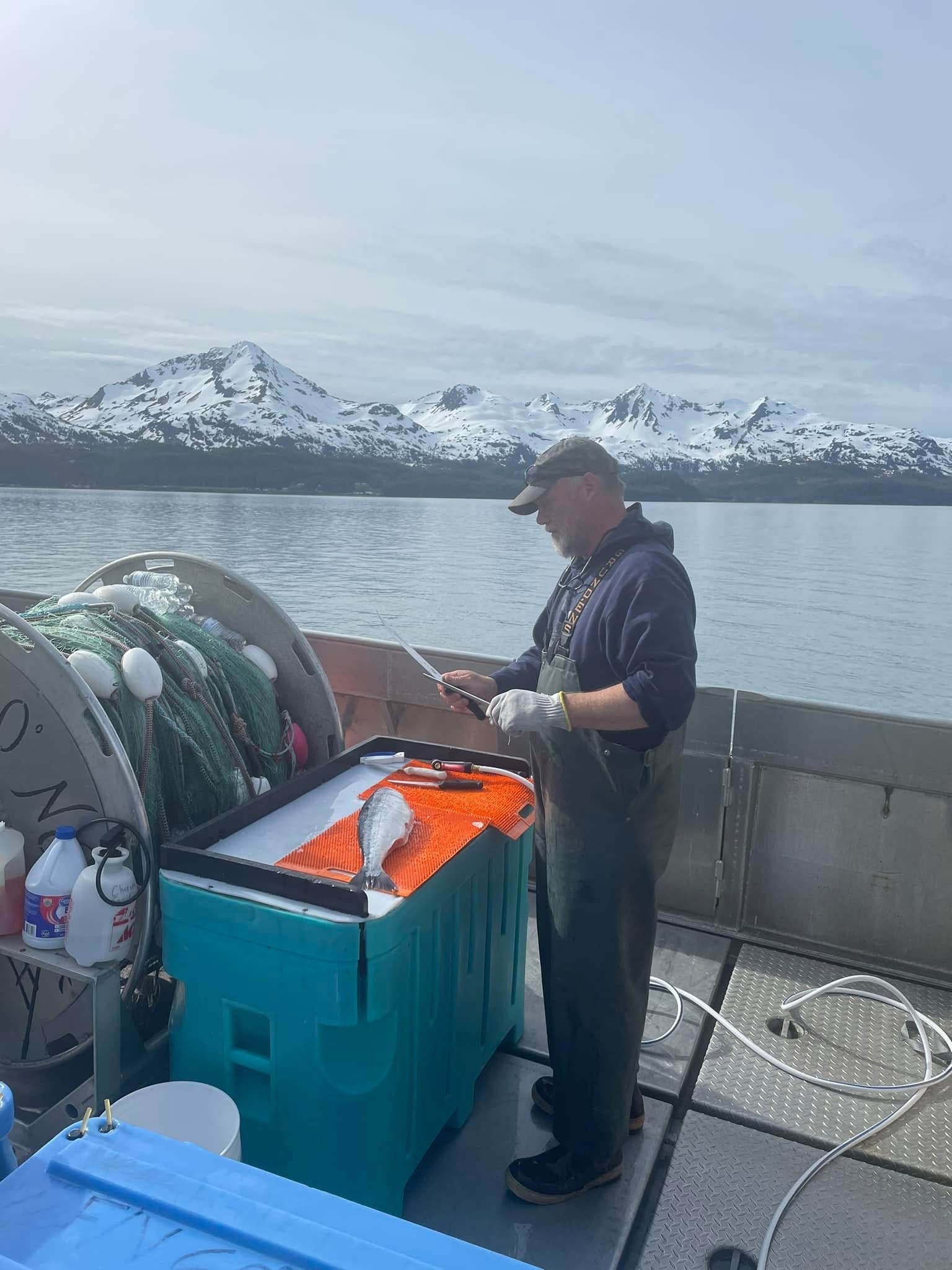 Man on a boat with fishing equipment and mountains in the background